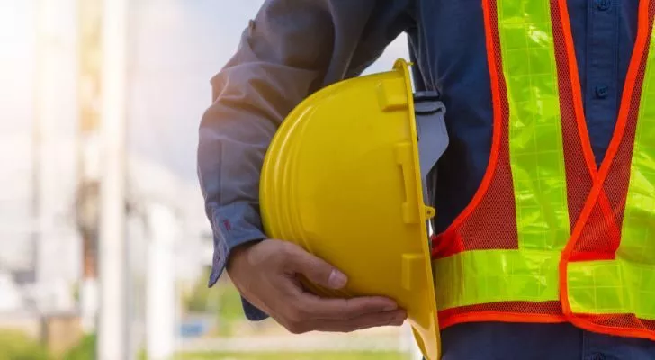 A construction worker wearing work clothes and holding a yellow hard hat